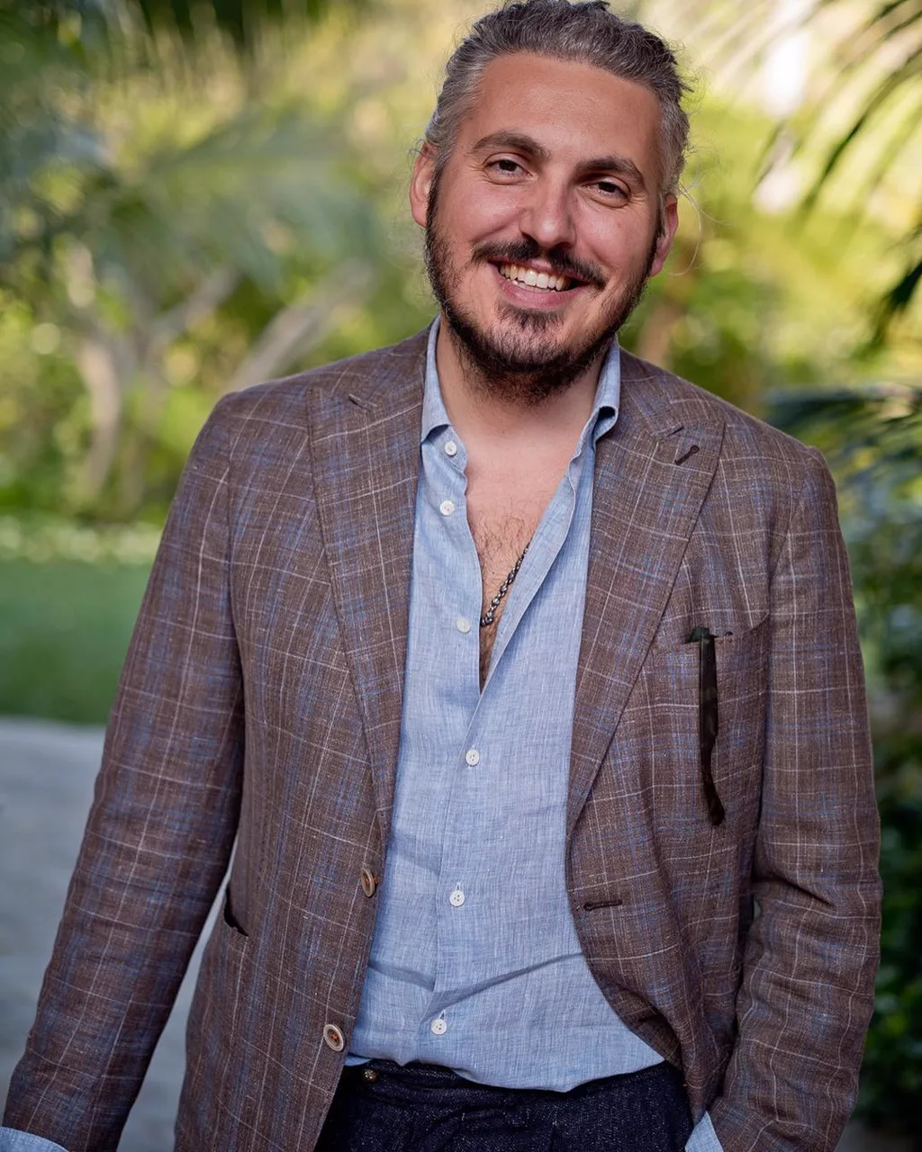 Matteo Perin smiling in golden light, in a brown check sport jacket over an open linen shirt