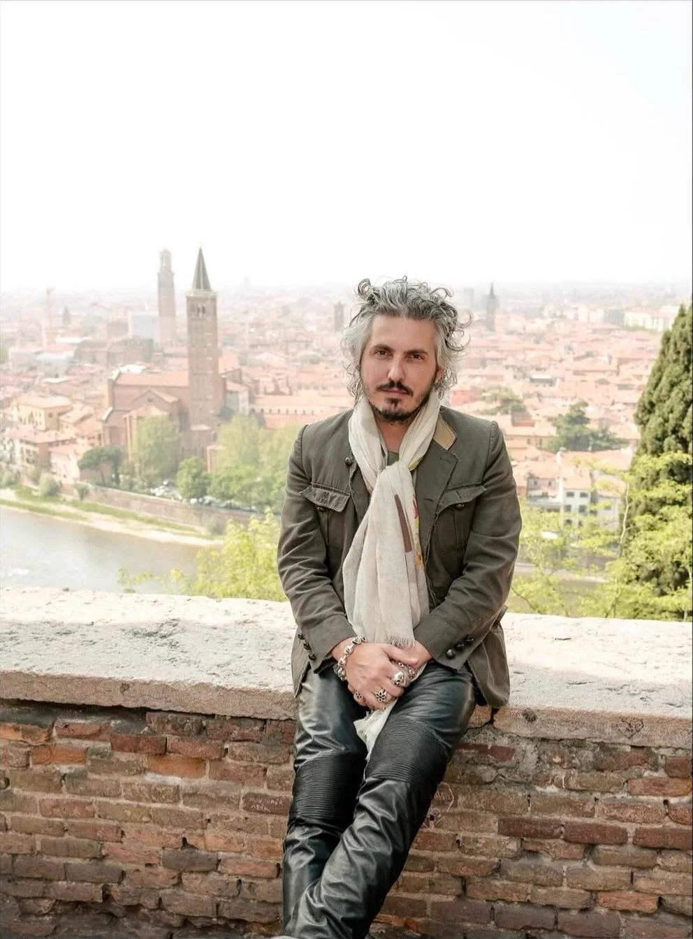 Matteo Perin seated on a brick parapet above the Verona skyline, the river and bell towers behind him