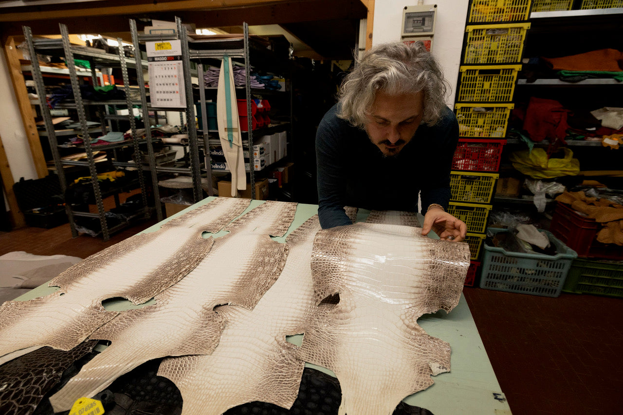 Designer examining high-quality crocodile leather hides in an artisan workshop, surrounded by tools and materials.