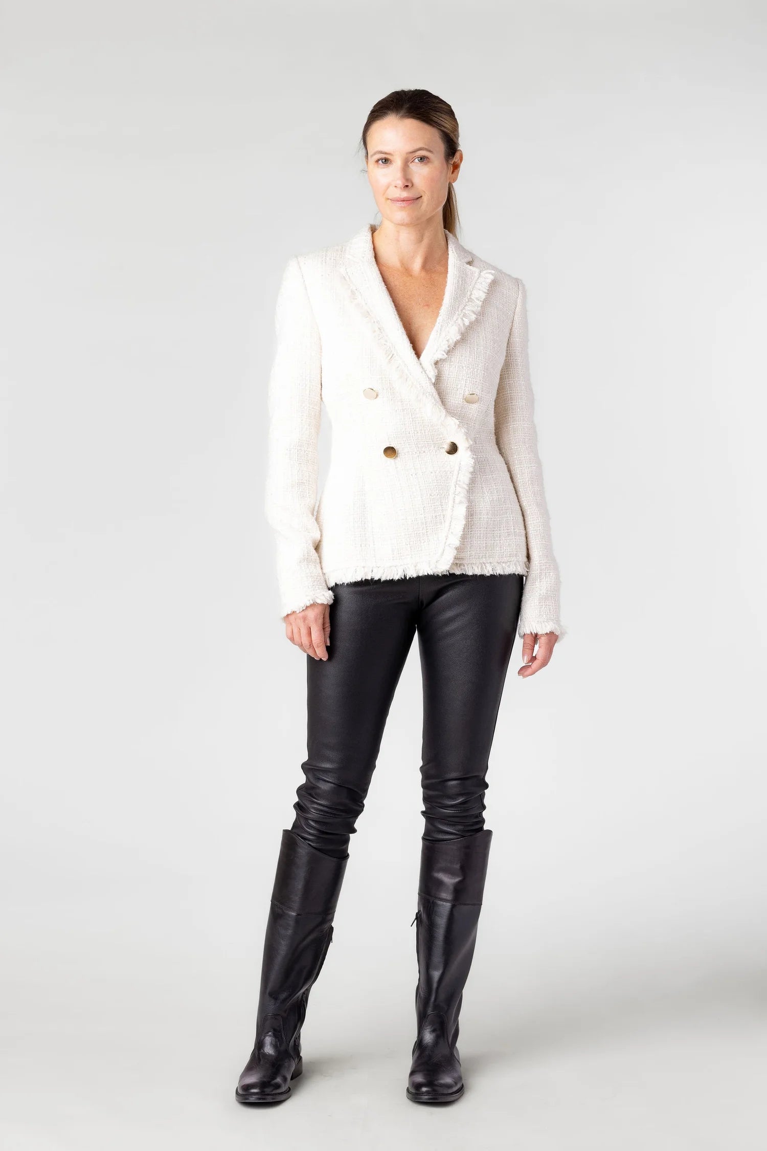 Woman wearing a white blazer and black leather pants on a white background
