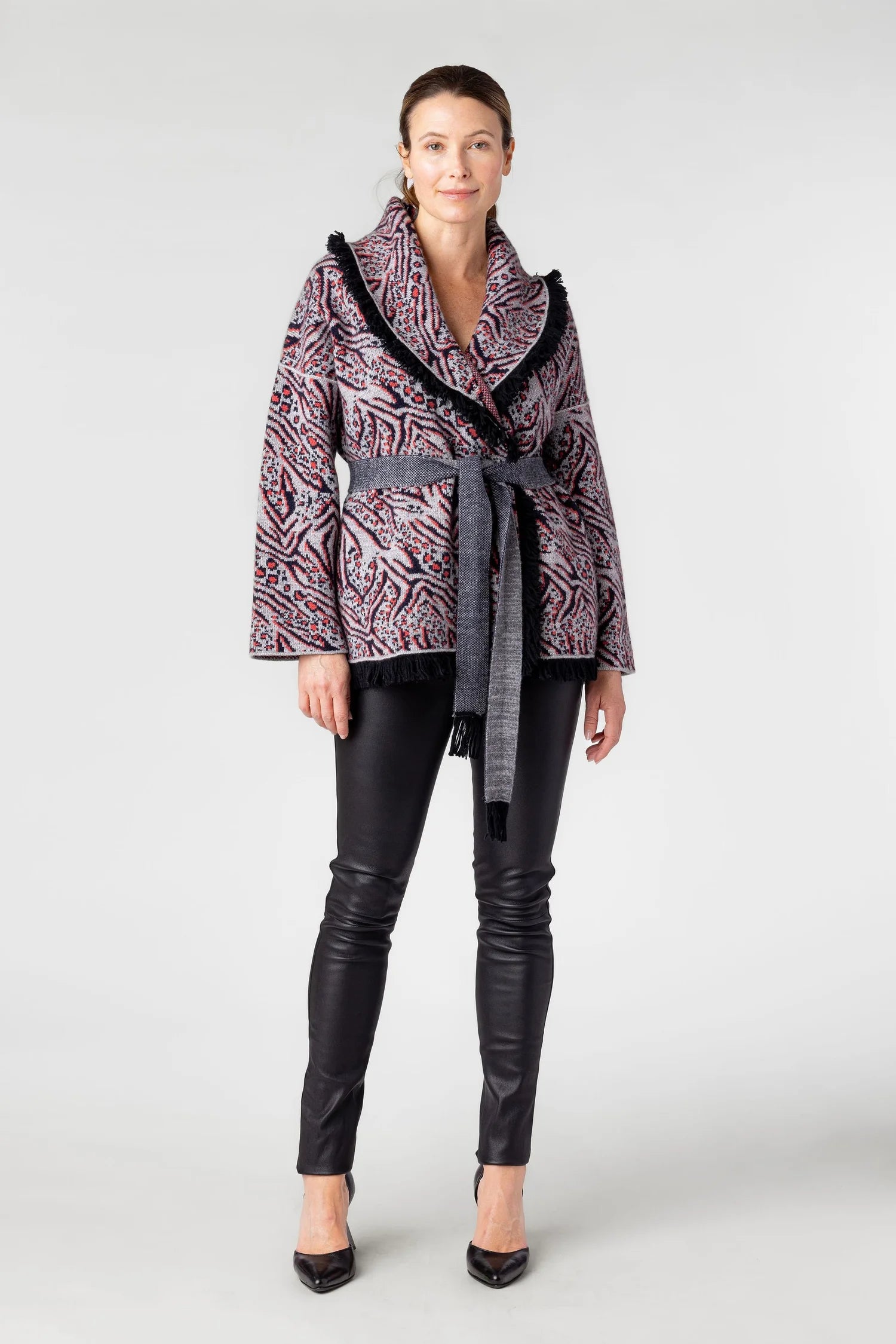 Woman wearing a patterned jacket with a belt and black pants on a white background