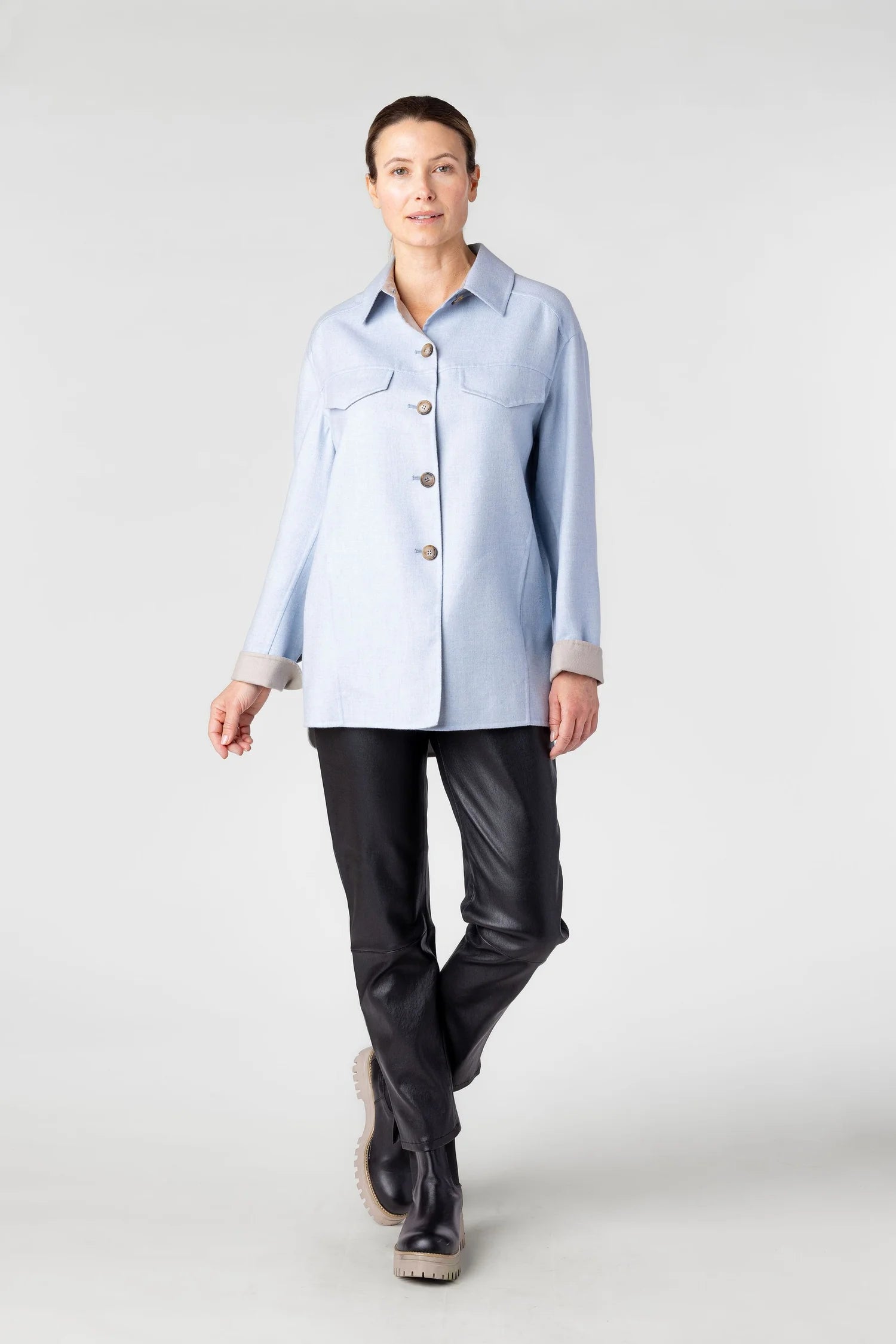 Woman wearing a light blue denim shirt and black pants on a white background