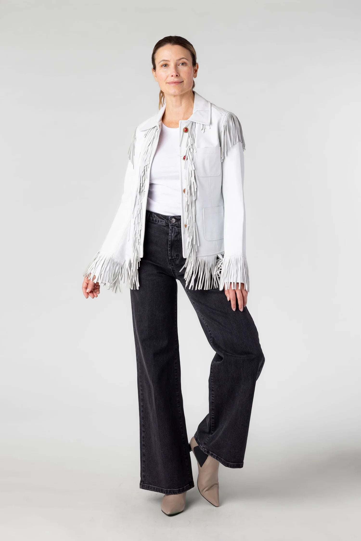 Woman wearing a white fringed jacket, white shirt, black pants, and beige shoes on a white background