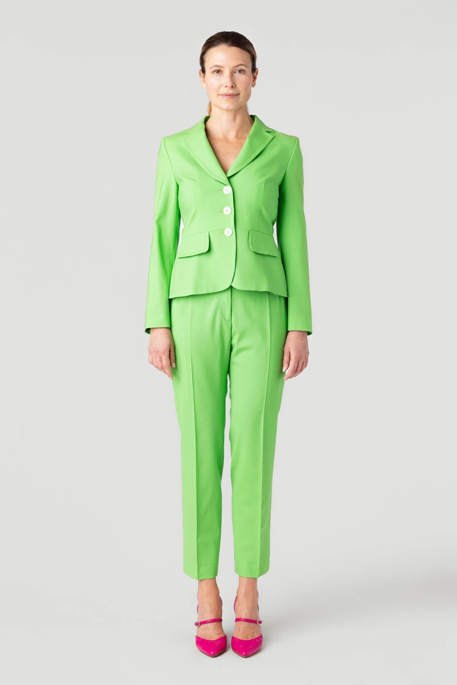 Woman wearing a bright green suit with pink shoes on a white background