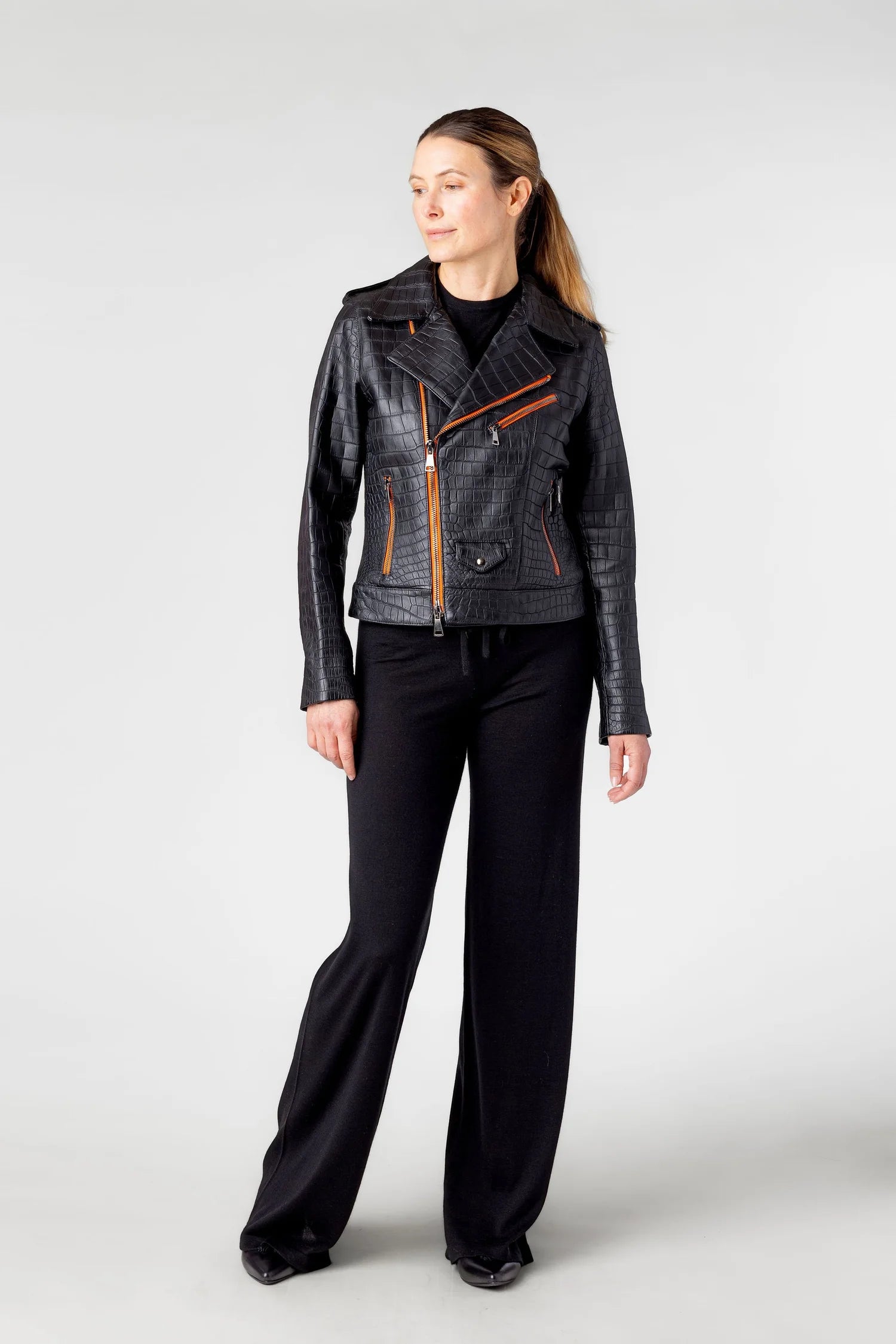 Woman wearing a black leather jacket with orange accents on a white background