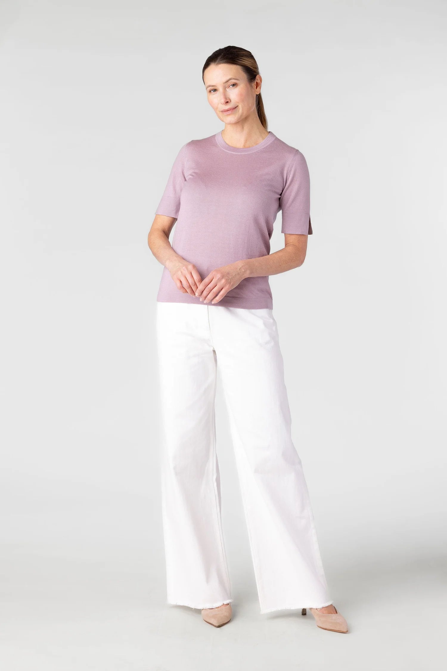 Woman wearing a light purple top and white pants on a white background
