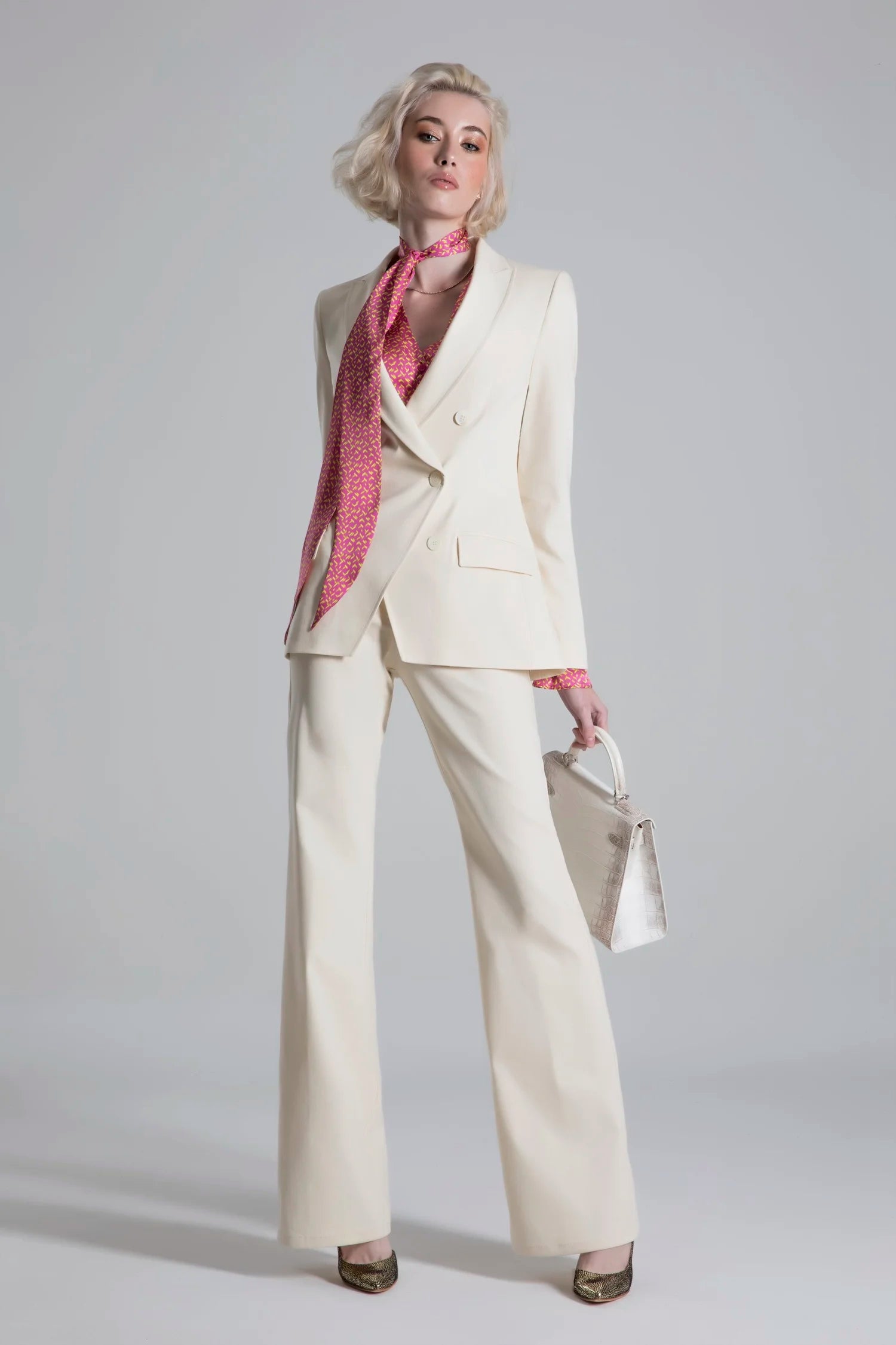 Woman wearing a white suit with a pink scarf against a gray background
