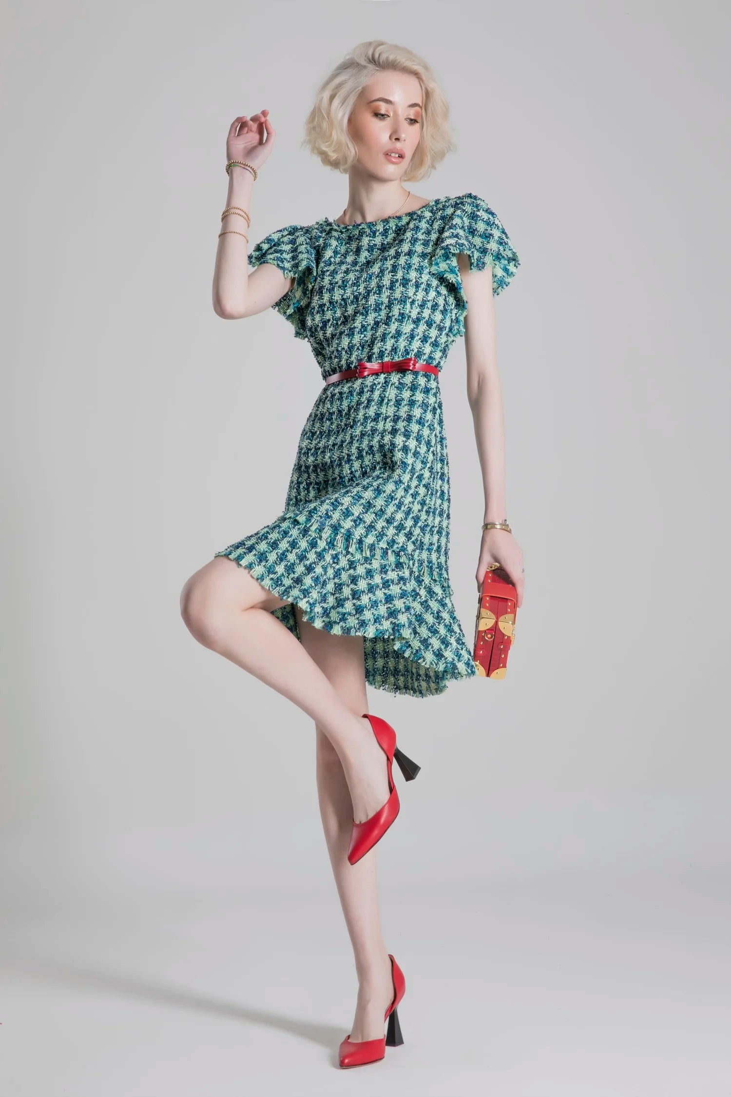 Woman wearing a patterned dress with a red belt and red shoes on a plain background