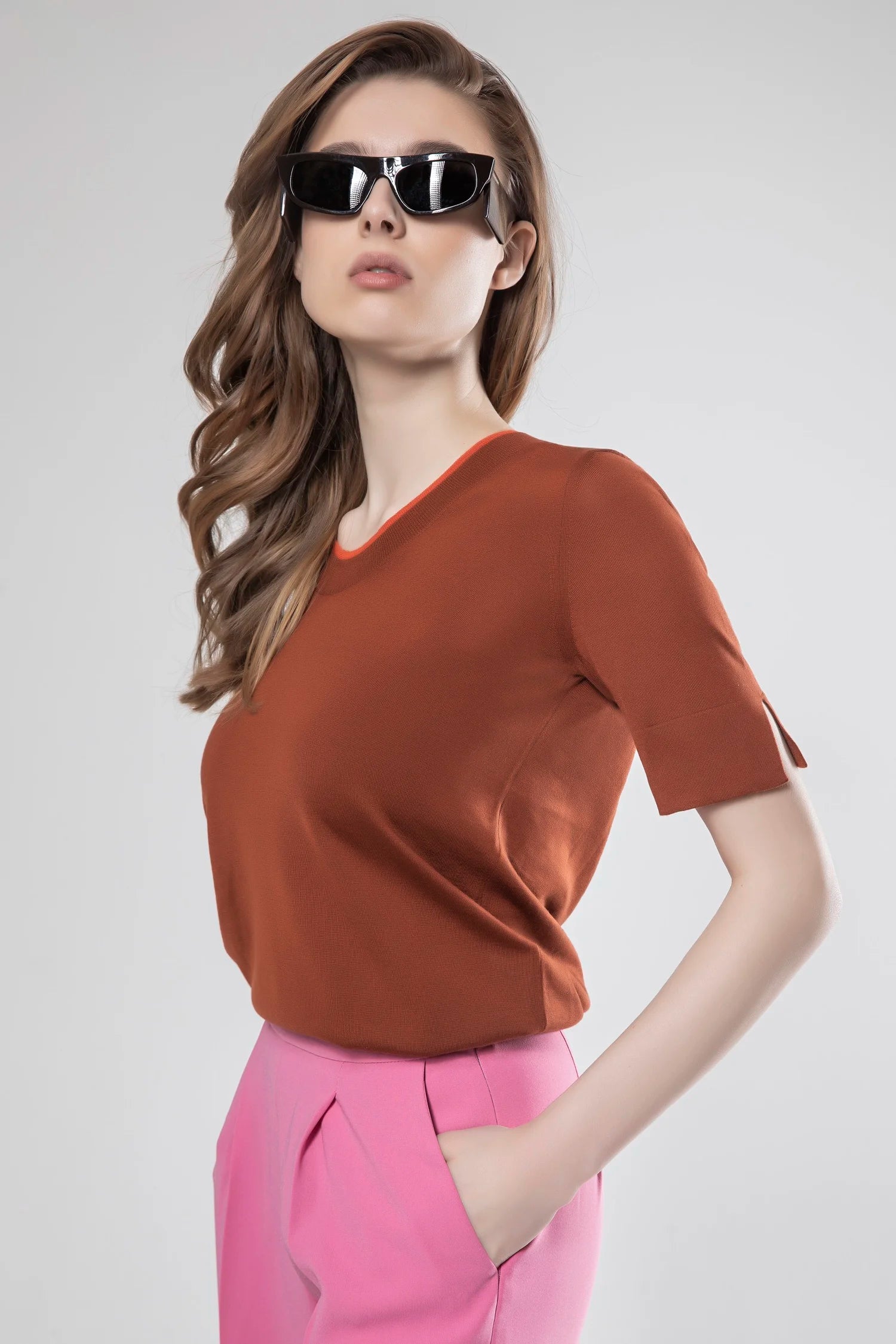 Woman wearing a brown top and pink pants with sunglasses on a white background