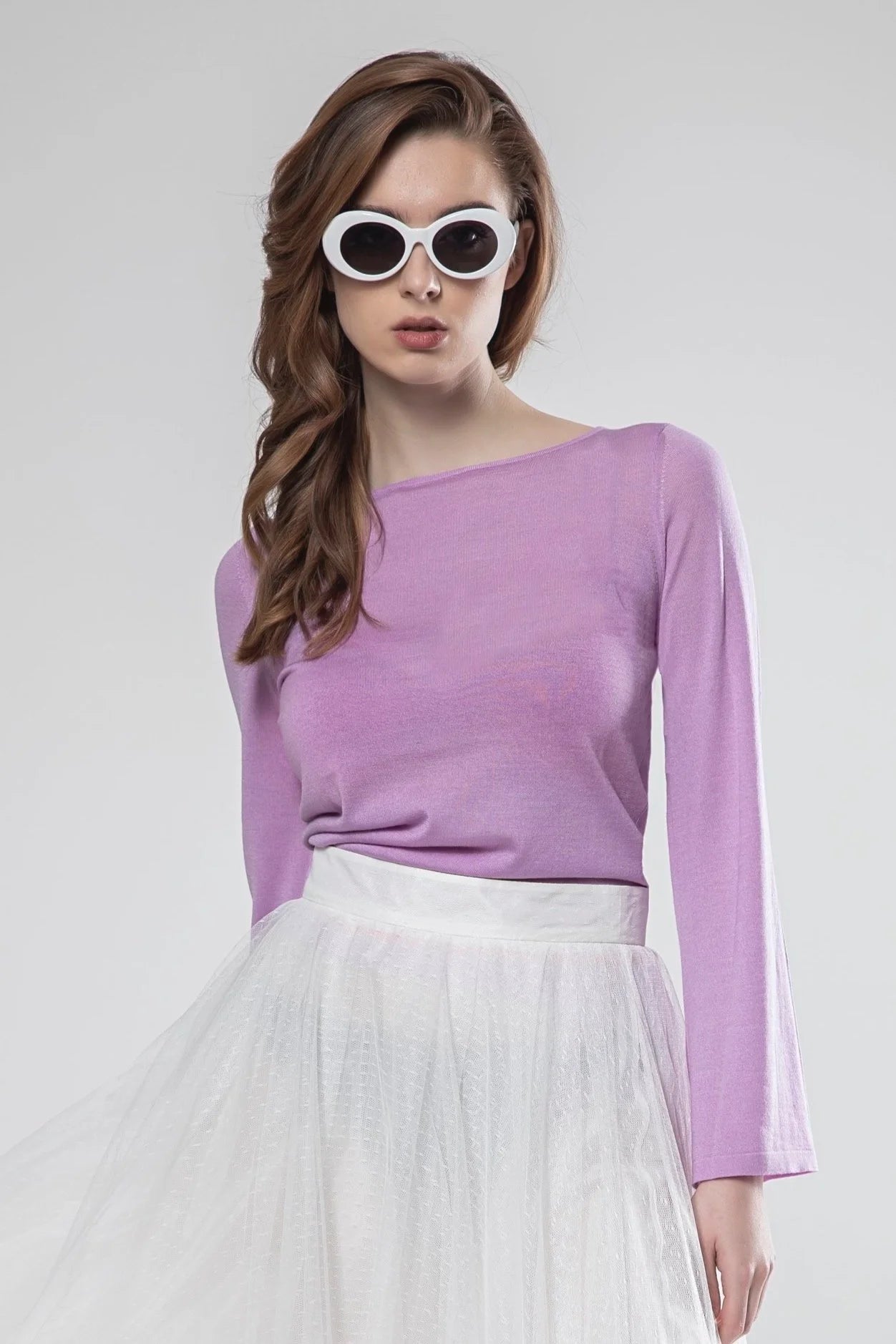 Woman wearing a purple long-sleeve top and white tulle skirt on a light gray background