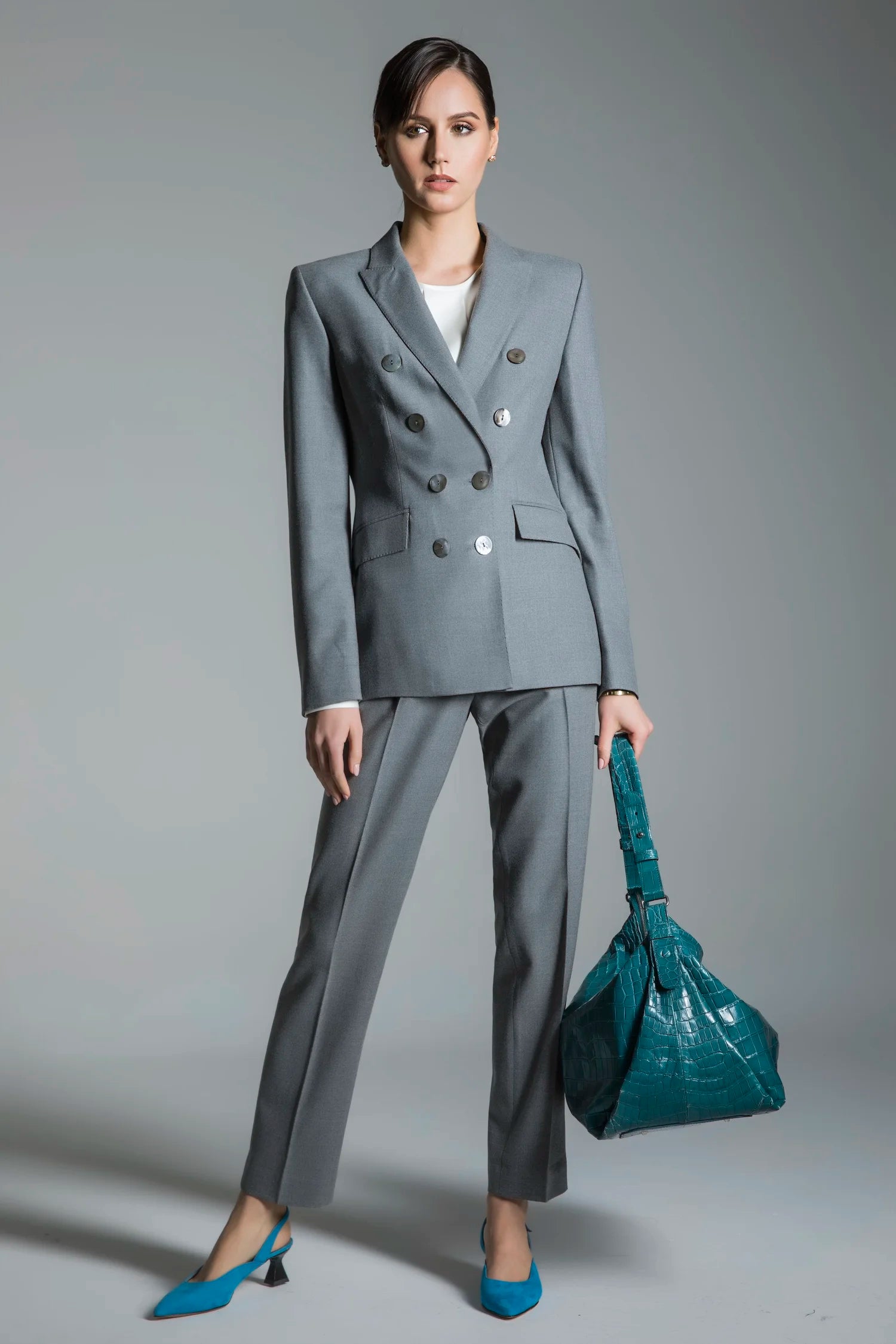 Woman in a gray suit holding a teal handbag against a gray background