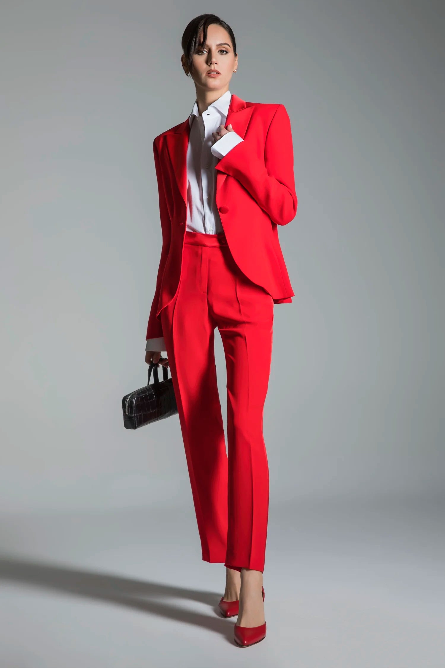 Woman wearing a red suit with a white shirt and red shoes on a gray background