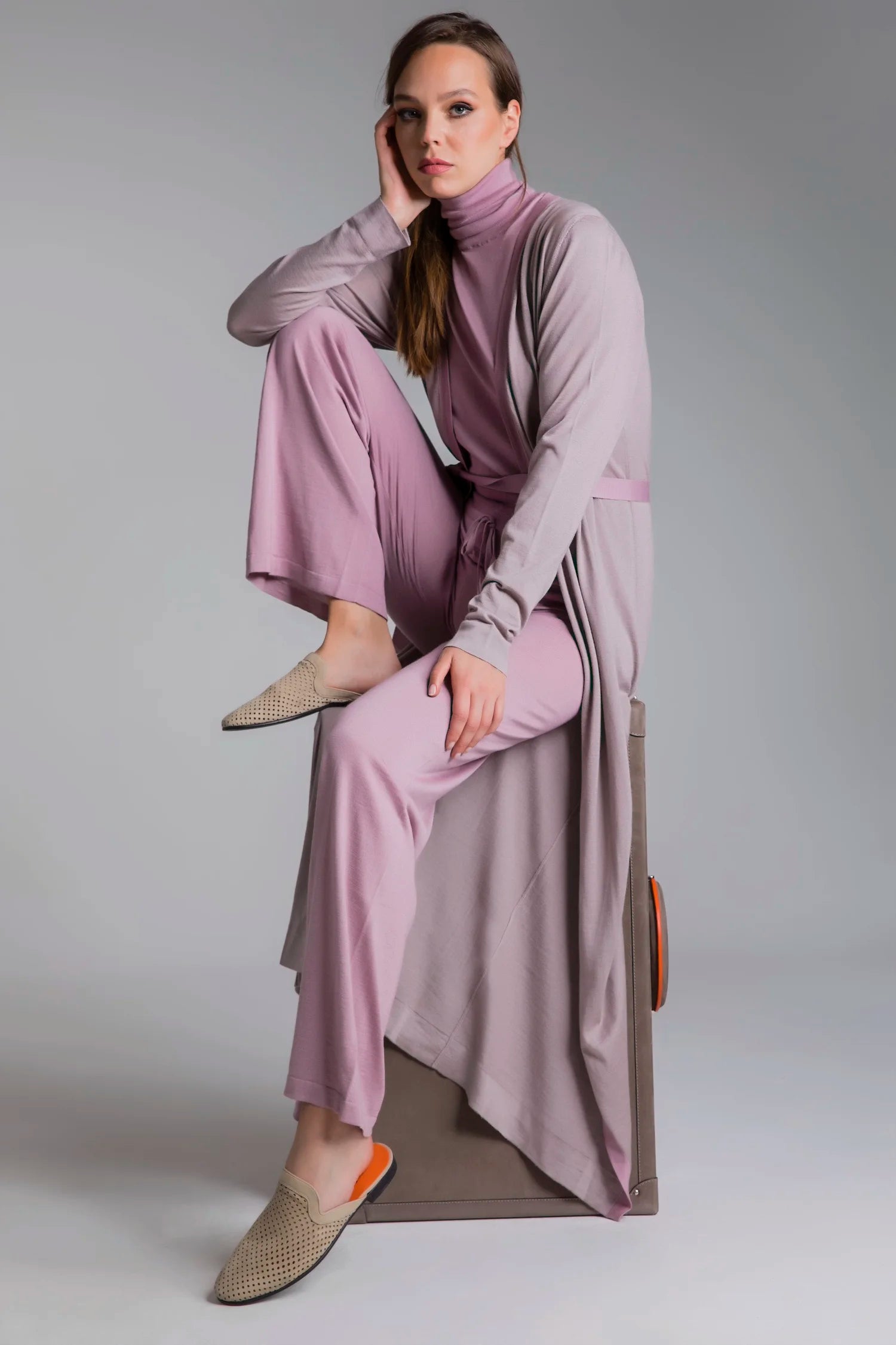 Woman in a pink outfit sitting on a chair against a gray background