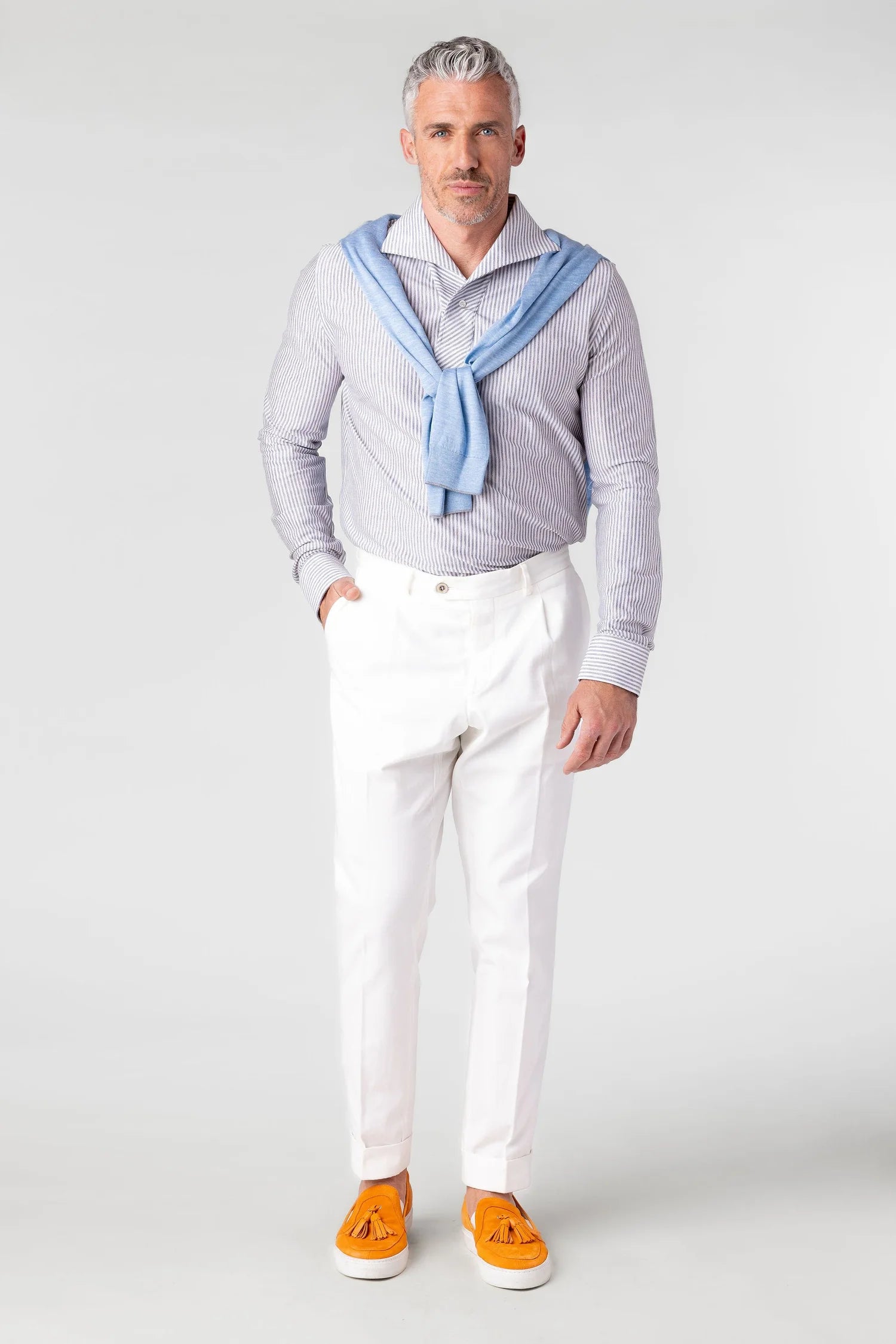 Man wearing a light blue shirt with a white collar, white pants, and orange shoes on a white background
