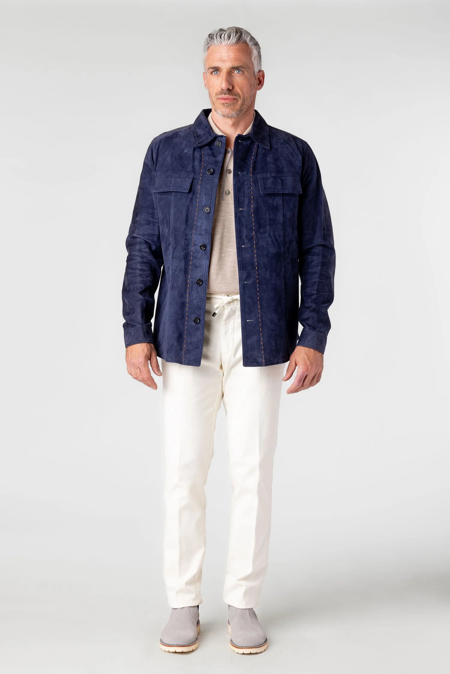 Man wearing a dark blue jacket, light shirt, white pants, and gray shoes on a white background