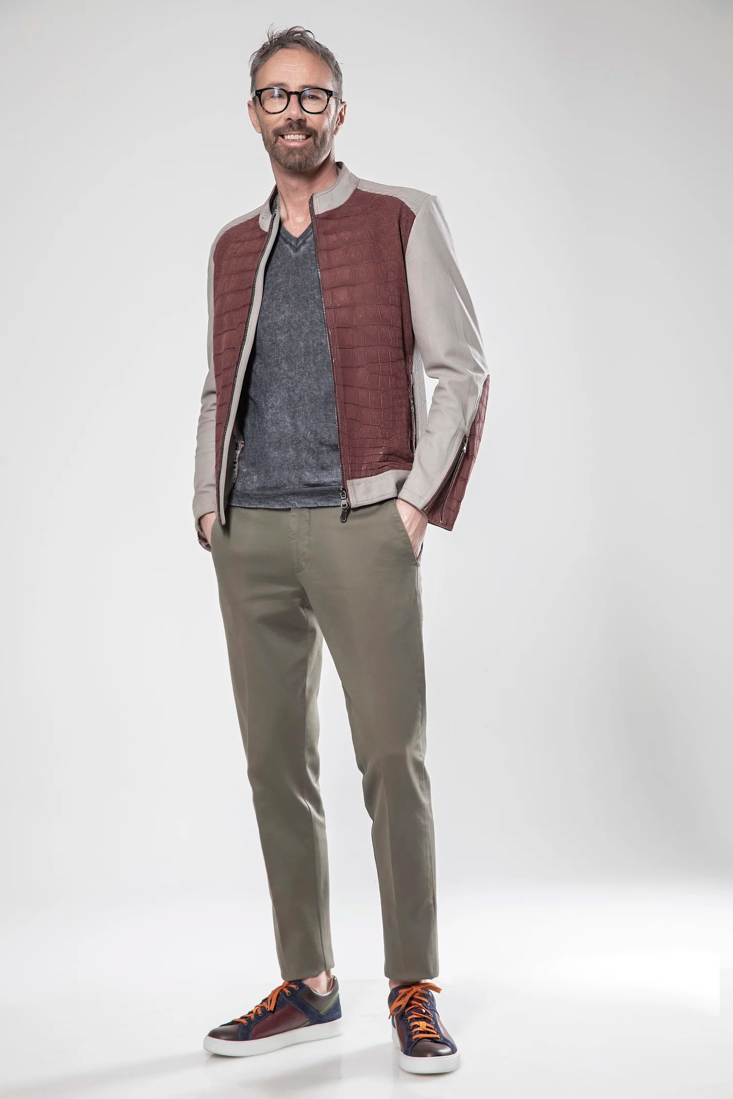 Man wearing a brown vest, gray shirt, beige jacket, green pants, and brown shoes on a white background