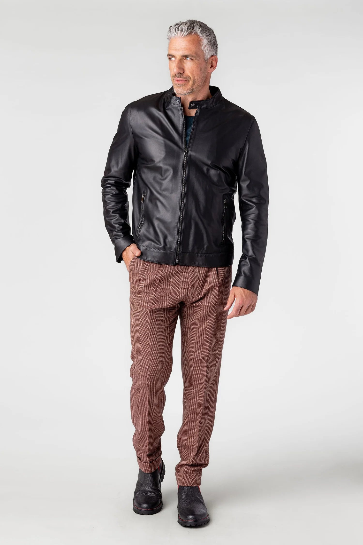 Man wearing a black leather jacket and brown pants on a white background