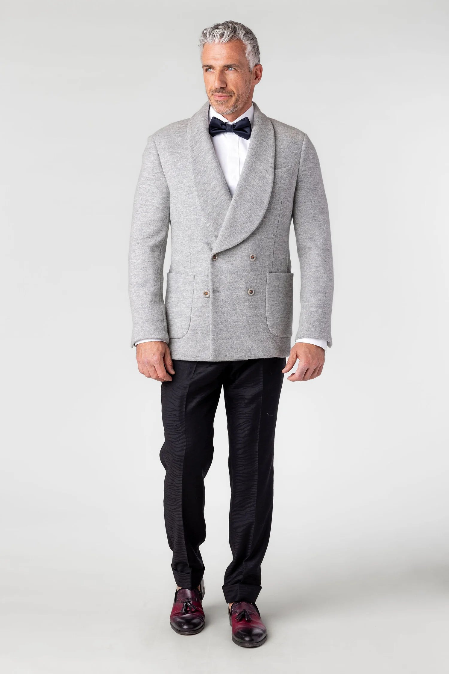 Man wearing a gray coat, black bow tie, white shirt, and dark pants on a white background