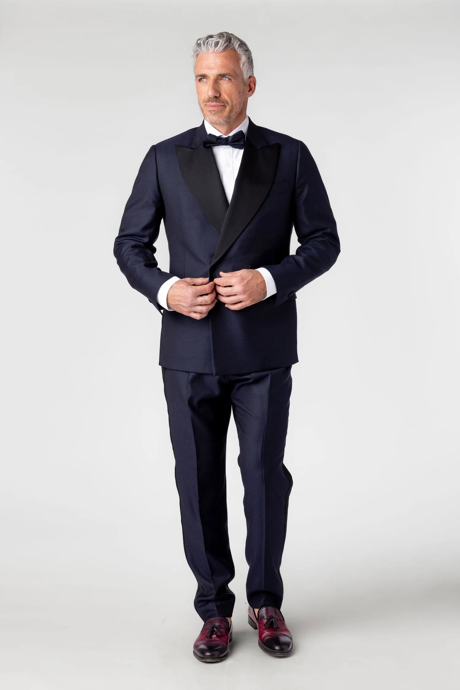Man wearing a navy tuxedo with a bow tie on a white background