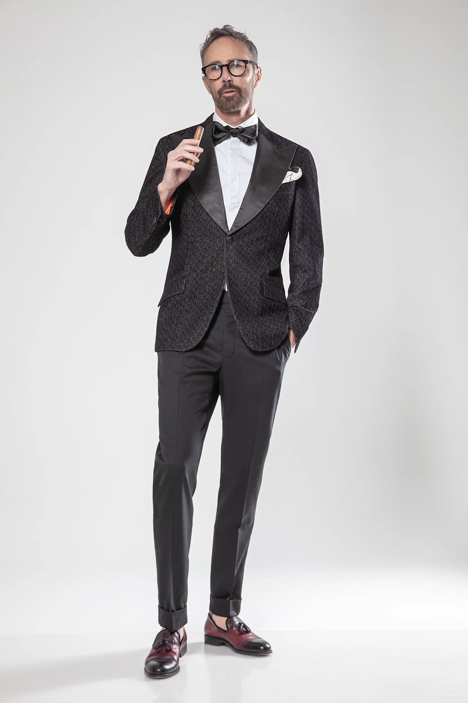 Man wearing a black tuxedo with a white shirt and bow tie on a white background