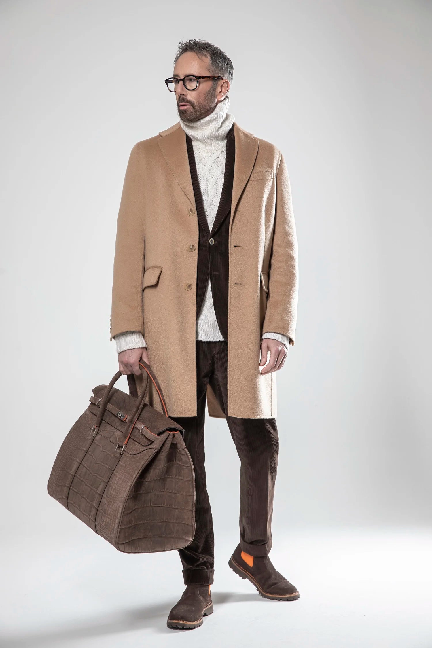 Man in a stylish outfit with a beige coat and brown bag on a white background