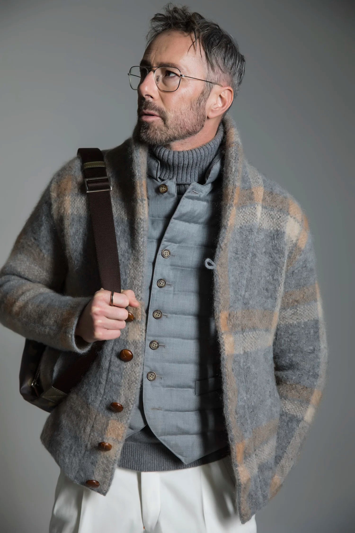 Man wearing a patterned coat over a gray sweater with a plain background