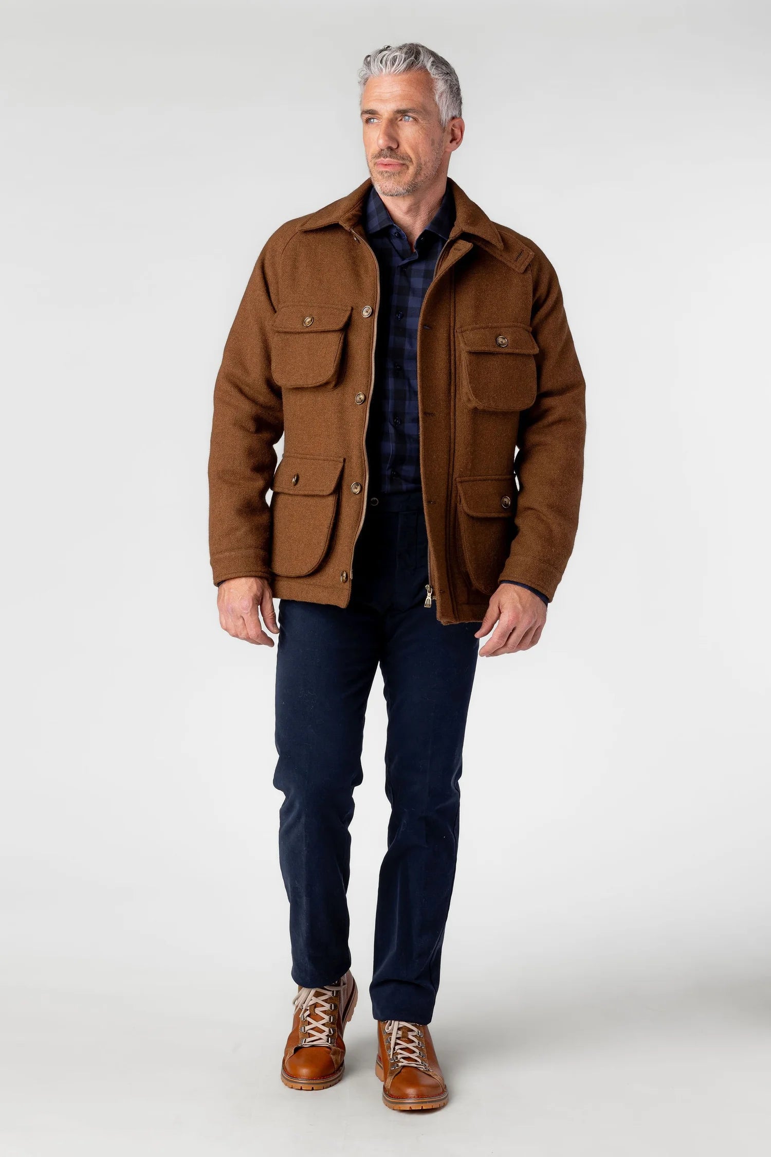 Man wearing a brown jacket, dark shirt, and jeans on a white background