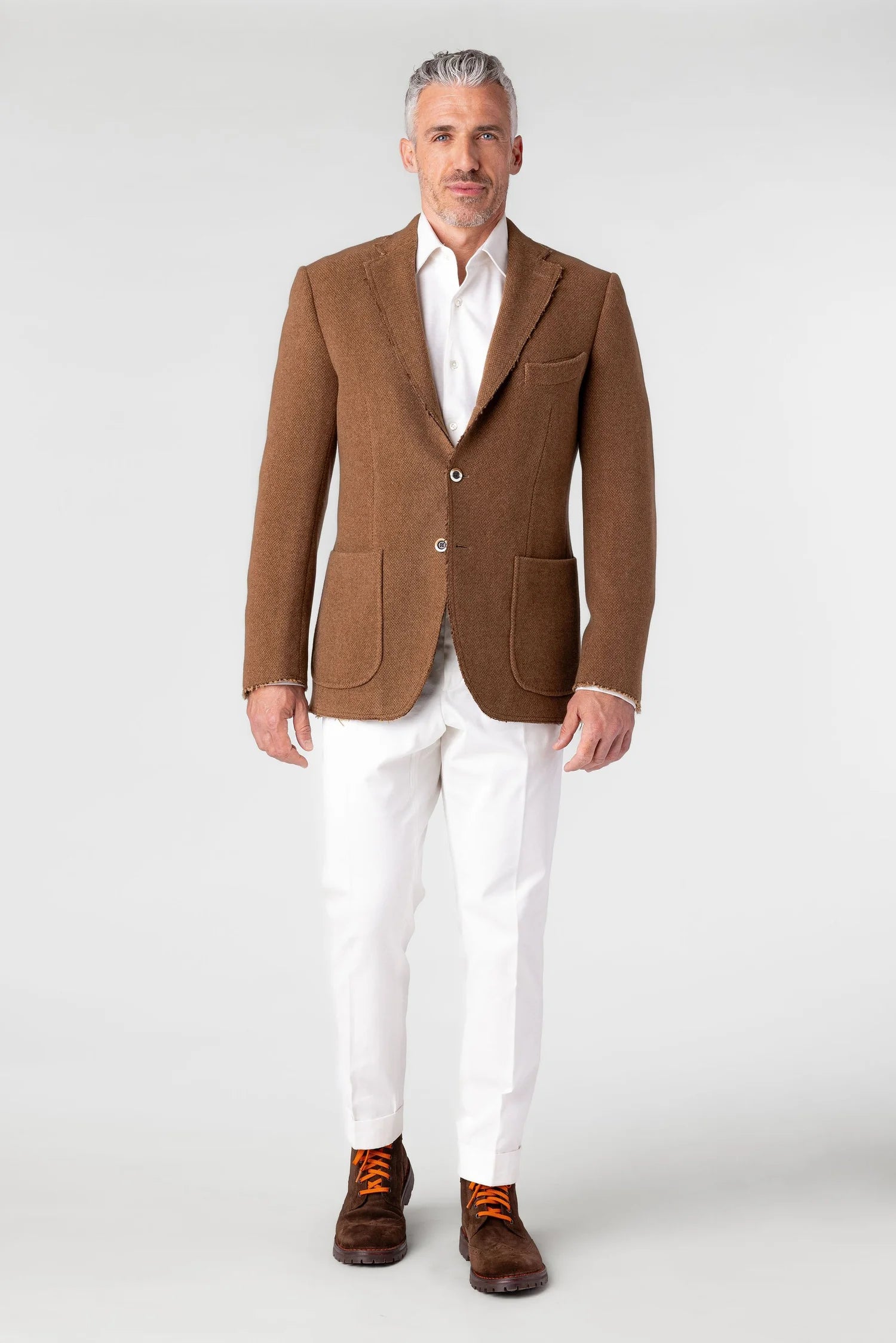 Man wearing a brown blazer, white shirt, and white pants on a white background