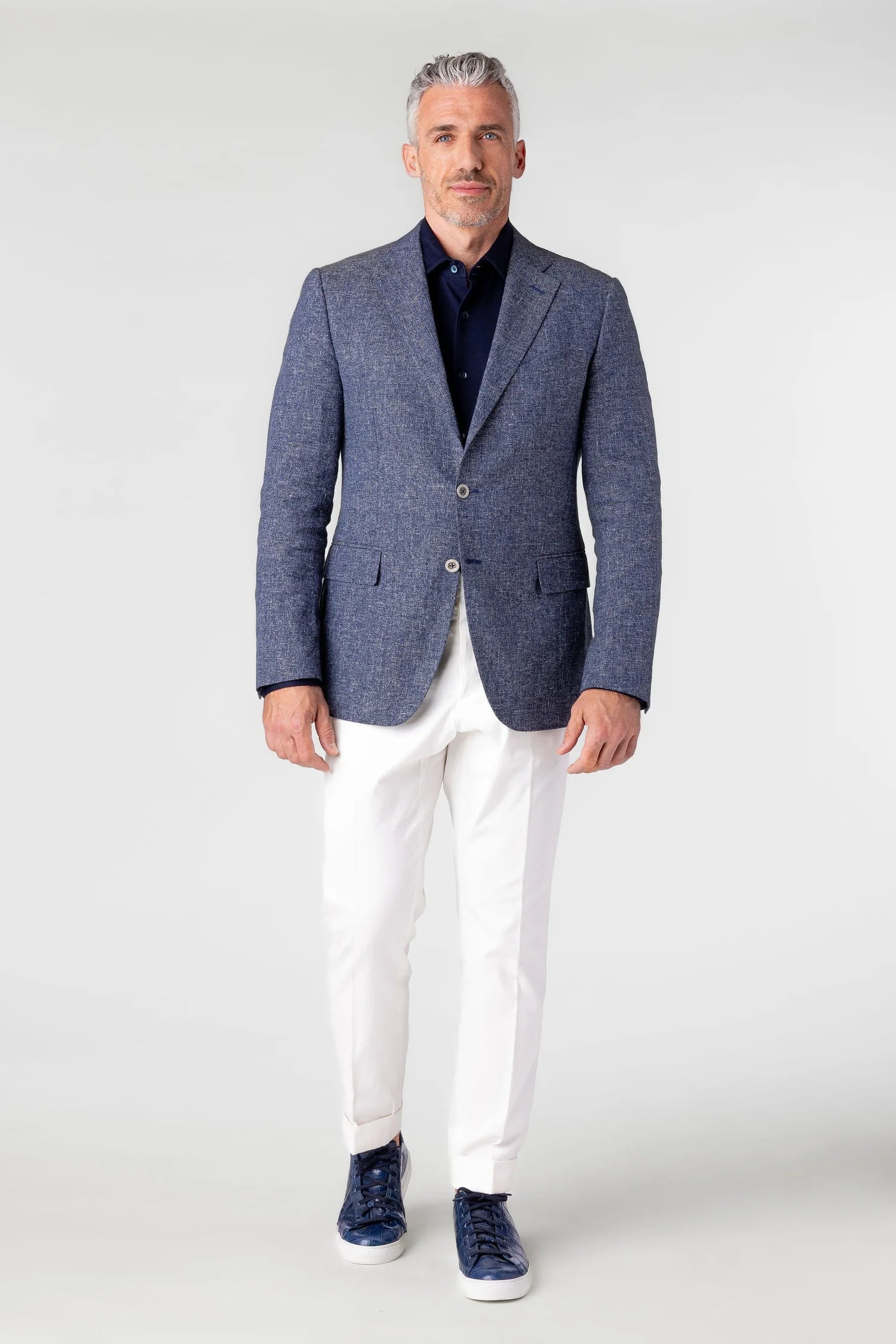 Man wearing a blue blazer, white pants, and navy shoes on a white background