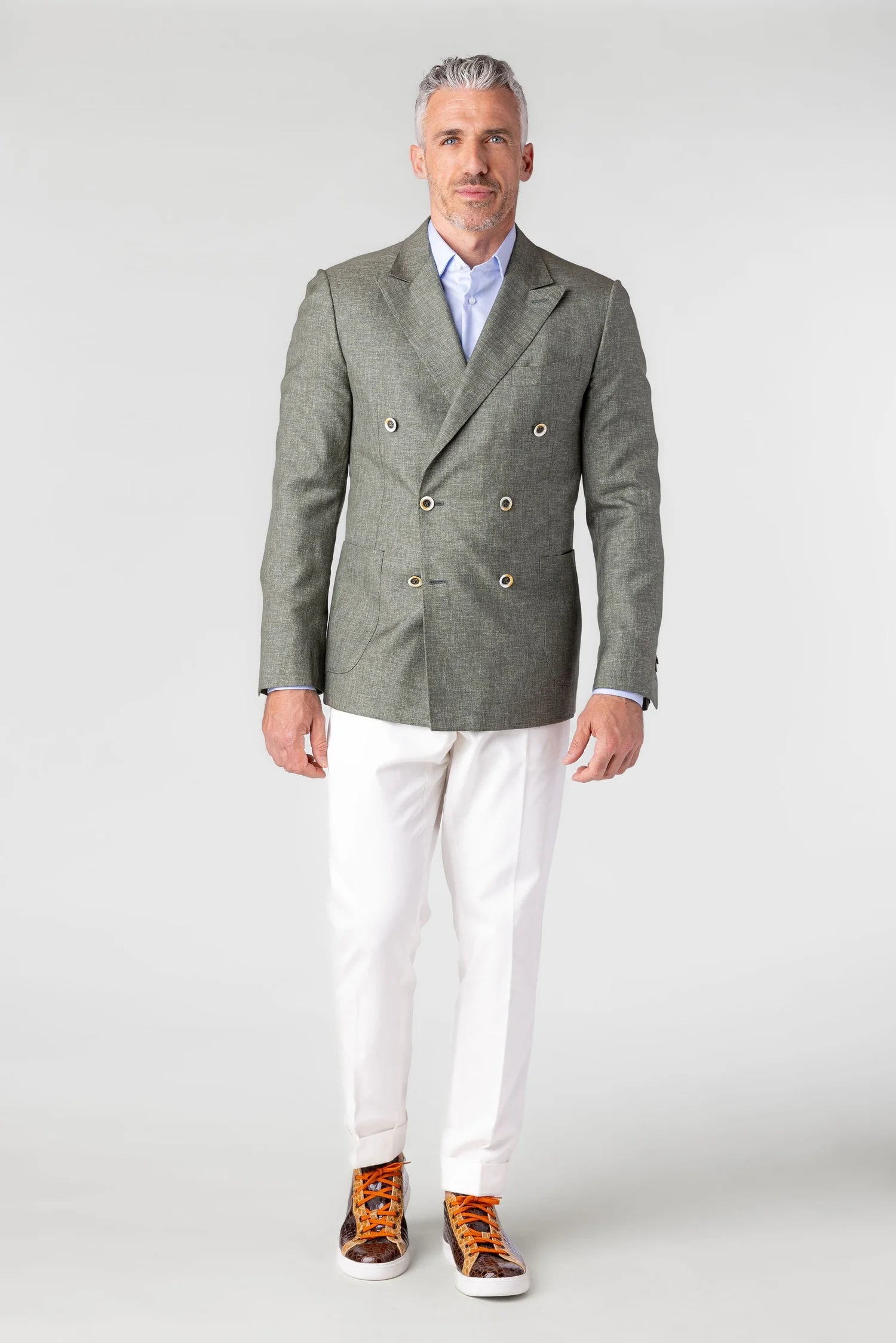 Man wearing a green blazer, white shirt, and white pants on a plain background