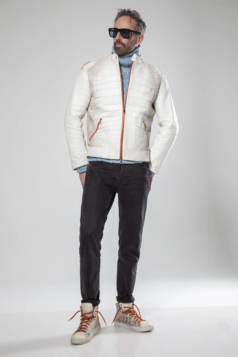 Man wearing a white puffer vest over a gray sweater, black pants, and brown shoes on a light gray background