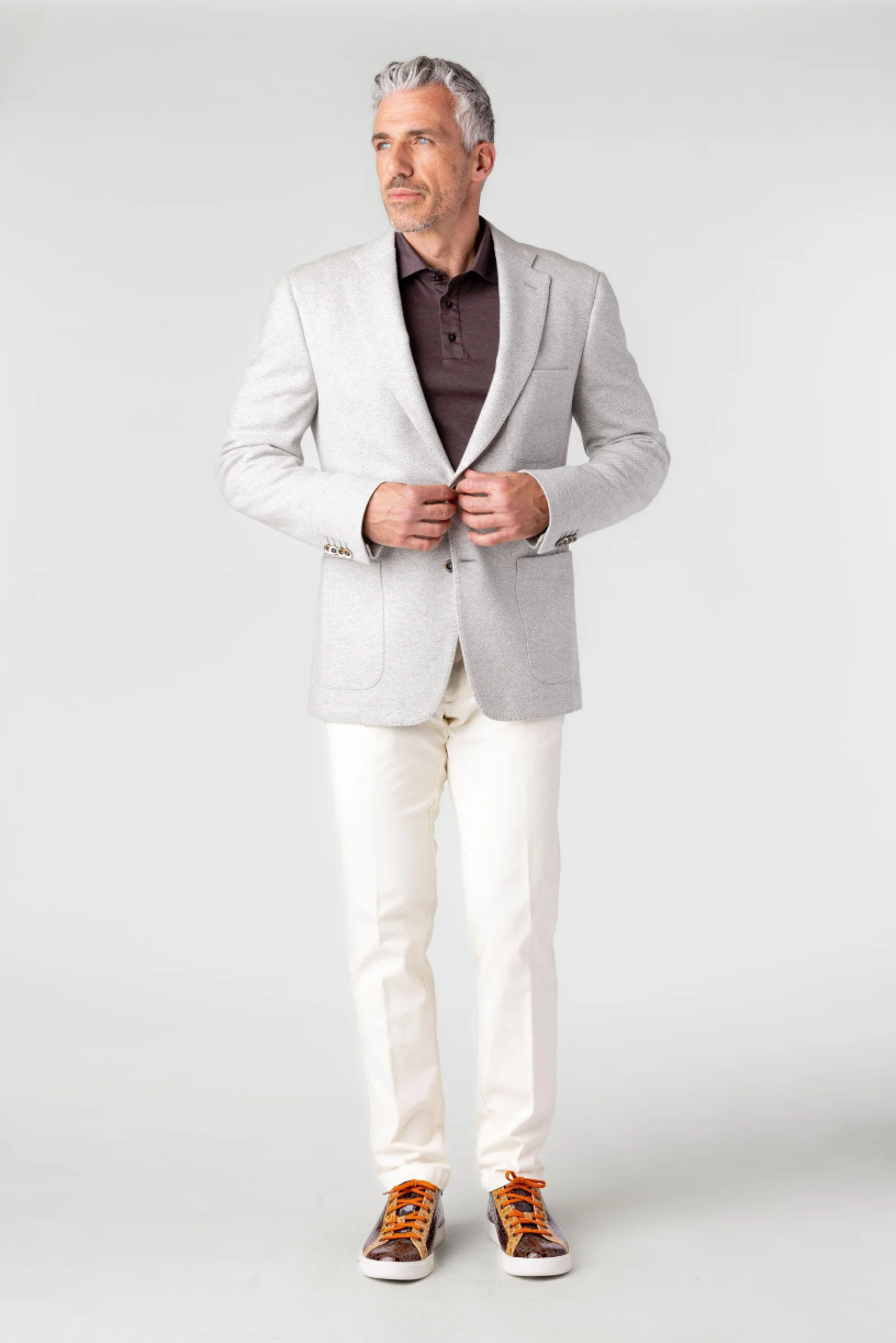 Man wearing a light gray blazer, white pants, and brown shoes on a white background